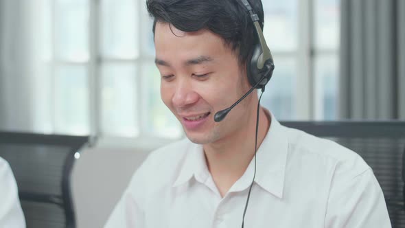 Close Up Of An Asian Man Call Centre Agent Wearing Headset Speaking To Customer