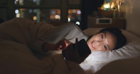 Woman use of cellphone and lying on bed at night