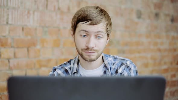 Sleepy tired young man sitting at office desktop with laptop, working and yawning in office