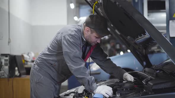 Professional Caucasian Maintenance Engineer Standing at Open Car Hood and Estimating Damage. Serious