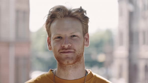 Portrait of Smiling Guy with Curly Red Hair Posing Outdoors