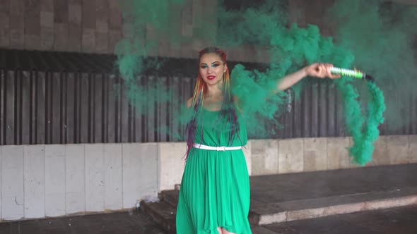 Cute Girl in a Green Dress with African Braids and Colorful Makeup Posing with Bright Green Smoke on