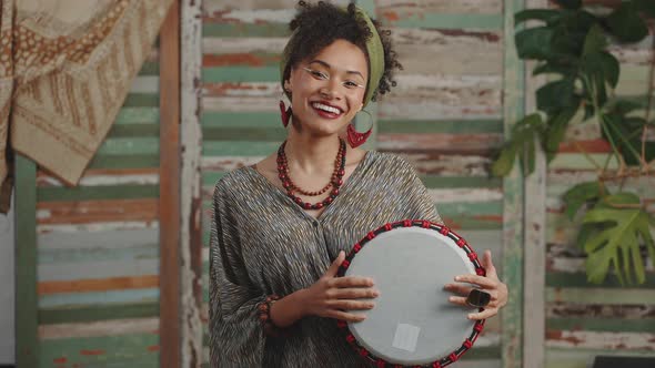 Young Happy Stylish African American Woman Playing on Djembe Drumming and Smiling to Camera