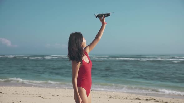 Gorgeous Brunette in Red Swimsuit on the Beach Launching Drone