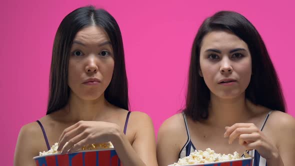 Two Women in Pajamas Eating Pop Corn and Attentively Watching Interesting Movie