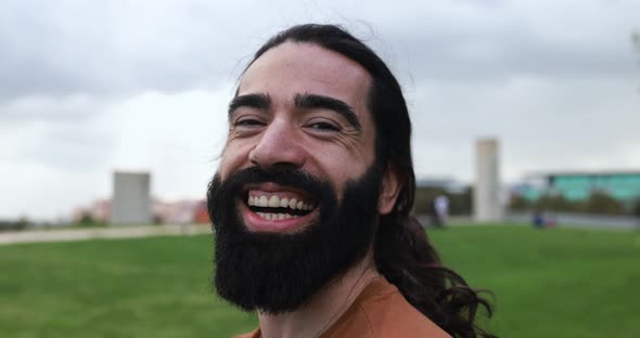 Happy hipster man with long hair laughing on camera at city park