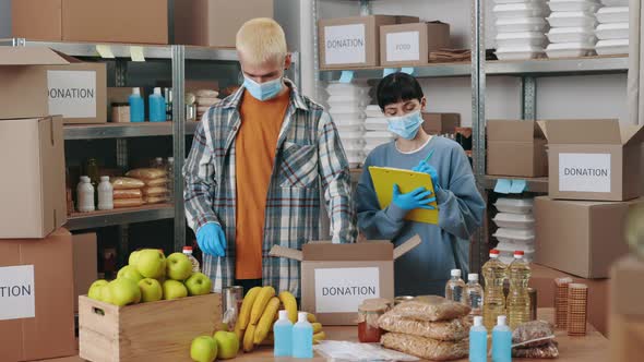 Man Packing Donation Box While Woman Using Clipboard