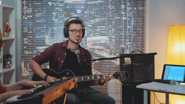 Recording Hit Song in Home Studio: Young Man in Headphone Singing and Playing Guitar