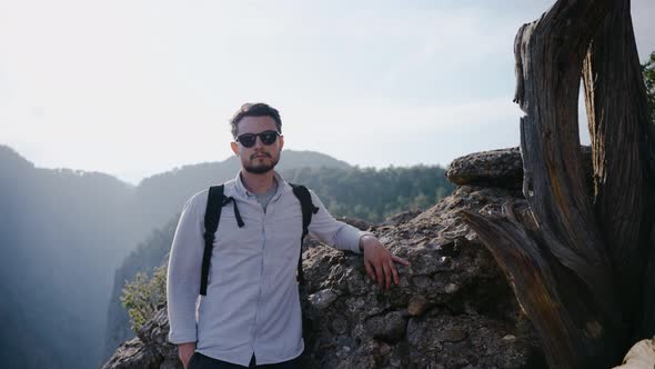 A Traveler in Sunglasses Stands Near the Rock and Looks at the Camera