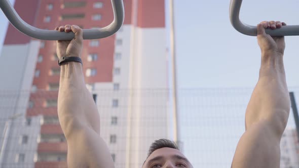 Young Muscular Man Pulls Himself Up on the Horizontal Bar of the City Playground