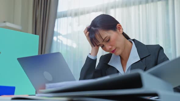 Exhausted Asian business woman worker feel tired and headache after look to paper work on table.