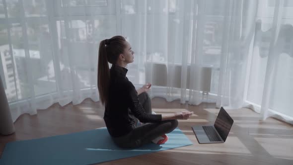 Young Woman Sits in Staff Easy Lotus Pose Near Laptop at Home Meditating Online Yoga Training
