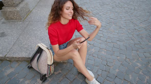 Happy Woman Sitting on Pavement and Using Phone