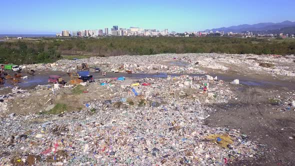 Drone view of city dump on background of sea, the city and the mountains.