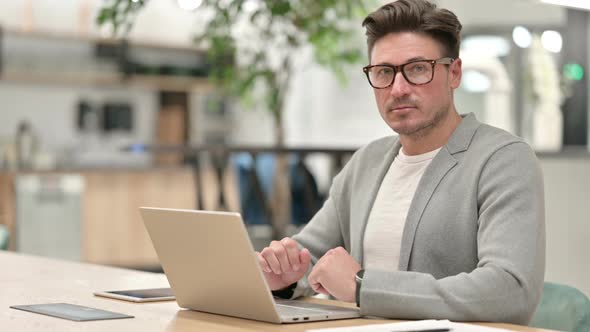 Serious Middle Aged Man with Laptop Looking at the Camera 