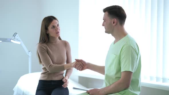 Smiling Caucasian Doctor Shaking Hands with Patient in Hospital Waving Goodbye to Woman Leaving in