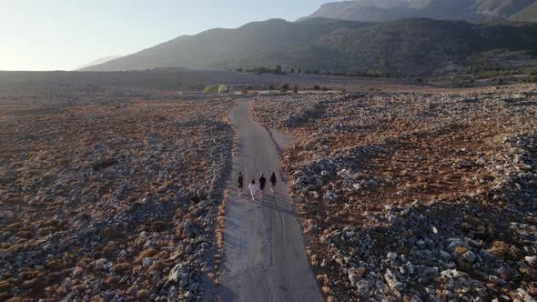 Four young tourists walking along empty rocky rural road in the countryside