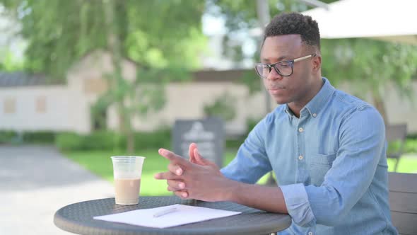 Sad African Man with Coffee and Documents Thinking in Outdoor Cafe