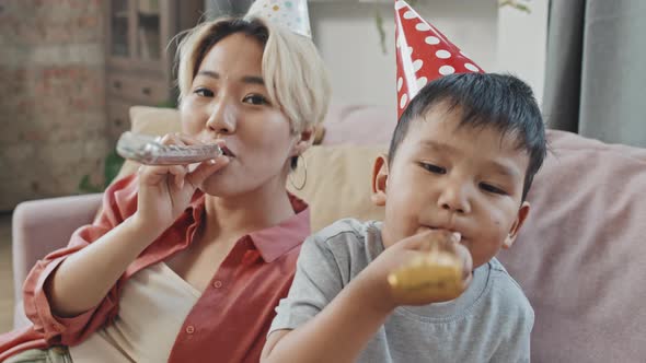 Asian Mother and Son Blowing Party Horns at Camera