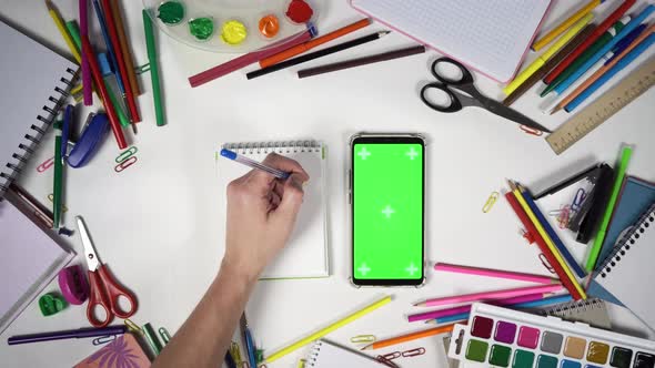 Man Take and Put Notebook with Smartphone on the Table Covered By School Supplies alt