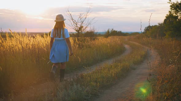 A Girl Walks Along a Rural Road at Sunset