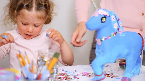 Step by step. Mother and daughter decorating paper mache unicorn with jewels and paper flowers