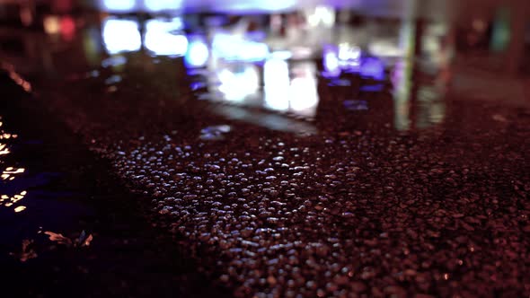 Heavy rain in city at night. Raindrops fall into puddle. Closeup macro perspective. Blurred cityscap