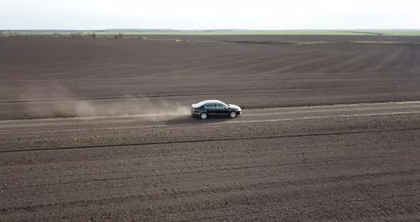 The Car is Racing Along the Road in the Countryside and Blowing a Dusty View From