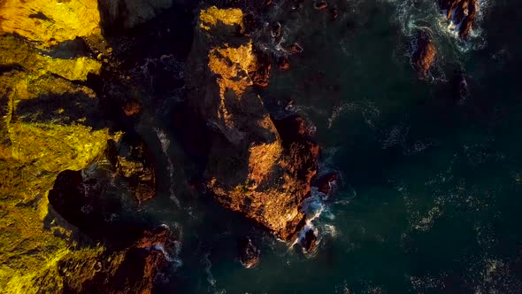 The last sunlight of day illuminates a blue ocean wave crashing into rocky cliffs in Big Sur Califor