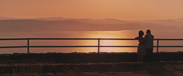 Young couple watching sunset above the lake from the viewing point. Wide shot