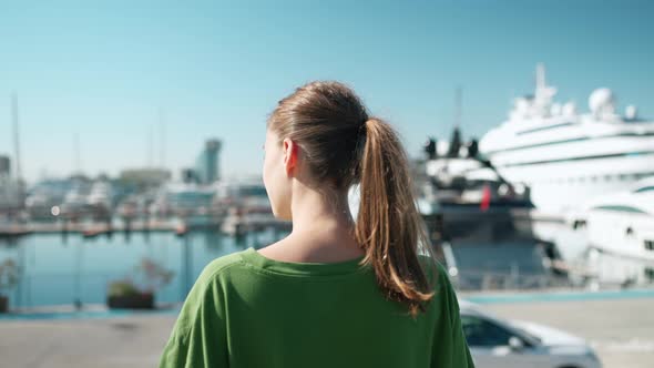 Blonde woman wearing green t-shirt looking at view on the seafront near yachts