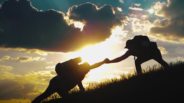 Silhouette of Helping Hand Between Two Climber. Two Hikers on Top of the Mountain, a Man Helps a Man