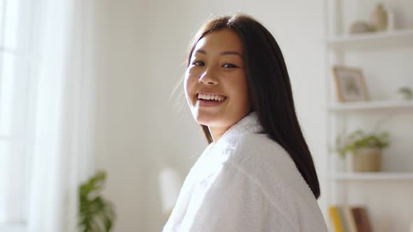 Young Peaceful Korean Woman Wearing White Bathrobe Smiling to Camera Posing at Home in Morning