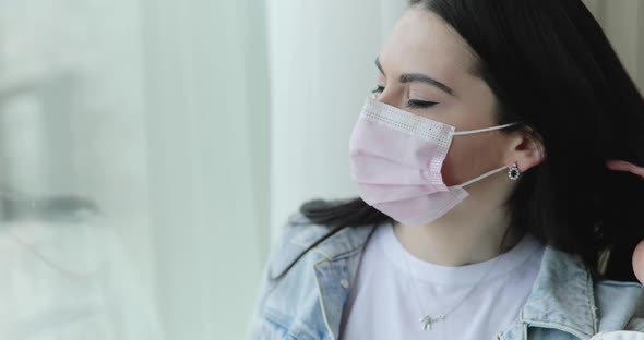 Young Girl in Surgical Mask Leaning on Window's Glass and Thinking in Home