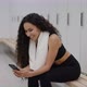 Young Sporty Woman Web Surfing Online in Social Media on Smartphone Resting at Gym Locker Room After - VideoHive Item for Sale