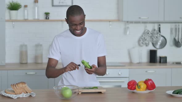 Healthy African Man Peeling Cucumber in Kitchen