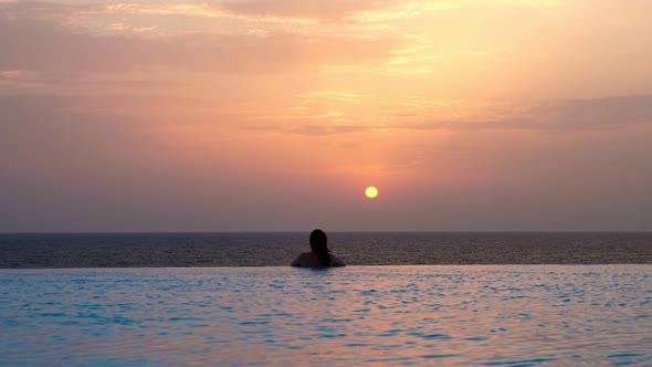 Back View, Silhouette of Woman, Is Relaxing in Water, on Edge of Outdoor Infinity Pool with