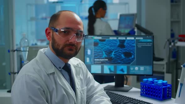 Portrait of Exhausted Scientist Man Looking at Camera Sitting in Front of Computer