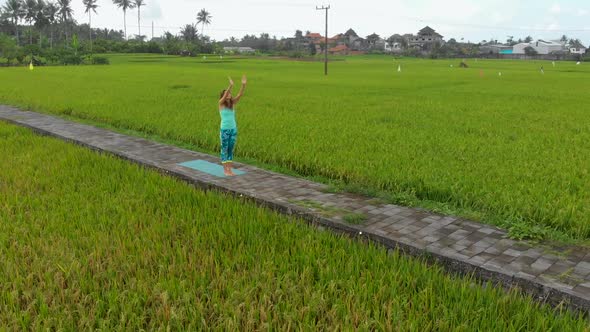 Aerial Slowmotion Shot of a Young Woman Practicing Yoga on a Beautiful Rice Field