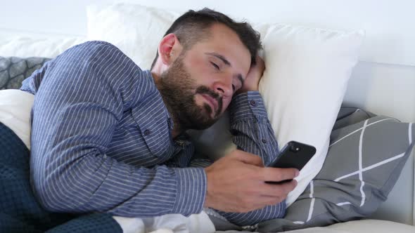 Man Using Smartphone while Lying on Side in Bed