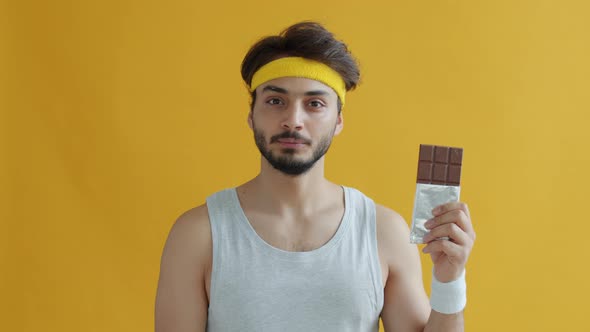 Portrait of Serious Arab Sportsman Smelling Chocolate Then Saying No to Sugar on Yellow Background