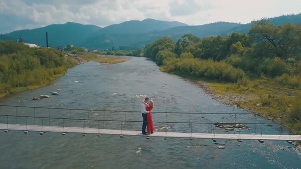 Couple Stands on Bridge Over a Mountain River. Love of Man and a Woman