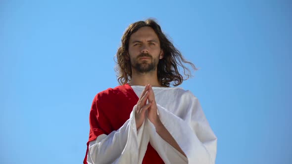 Jesus in Robe Praying Against Blue Sky Background, Asking God to Forgive Sinners