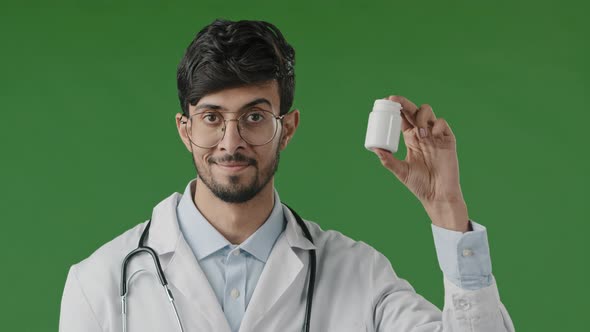 Indian Male Young Doctor Adviser in Medical Coat Standing Over Green Background Recommend at Camera