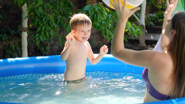 Happy Smiling and Laughing Little Boy Throwoing Colorful Beach Ball To His Mother in Swimming Pool