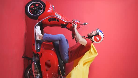 Portrait of a Man Riding a Scooter to a Theme Party Dressed in a Superhero Costume Isolated Red