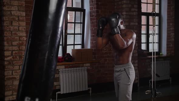 Black Athletic Shirtless Man Boxer Training Punching on the Punching Bag in the Gym