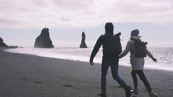 Young Couple Holding Hands and Running on Black Sand Beach in Iceland Slow Motion