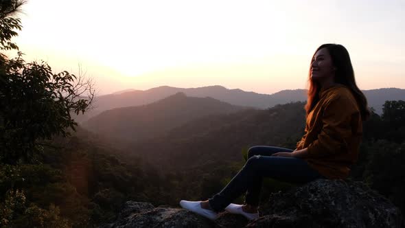 A female traveler sitting on the mountain peak and watching sunrise in the morning