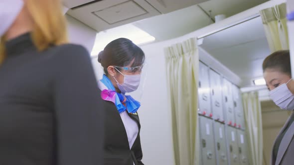 Flight attendants wearing face mask greeting passengers walking and coming on board in airplane.